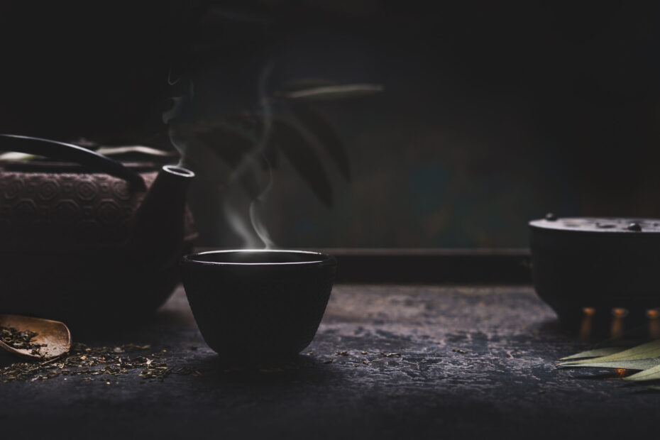 Dunkler Hintergrund mit asiatischer schwarzer Teekanne und Tasse heißem Tee mit Dampf auf dem Tisch