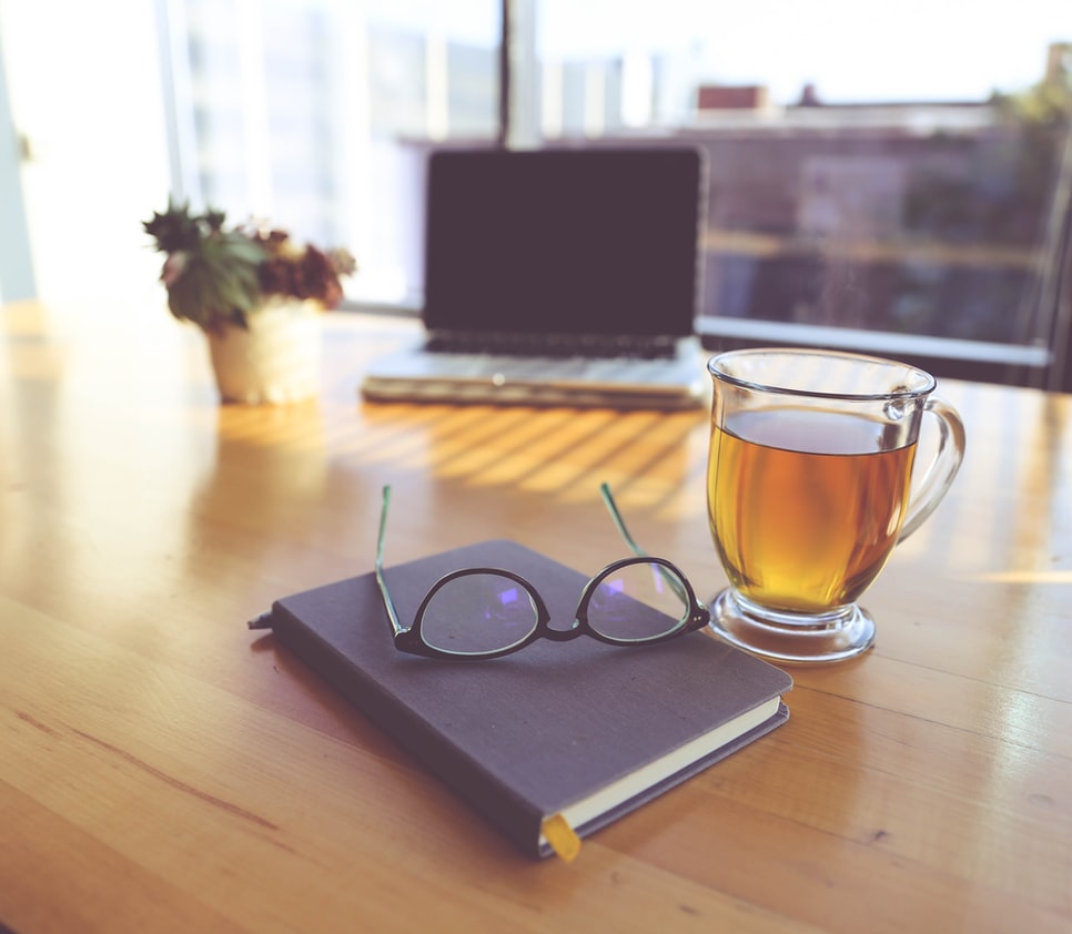 Schreibtisch mit Buch, Lesebrille, Laptop und einer Tasse Tee