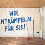 Leere Wohnung mit dem Schriftzug "Wir entrümpeln für Sie" an der Wand