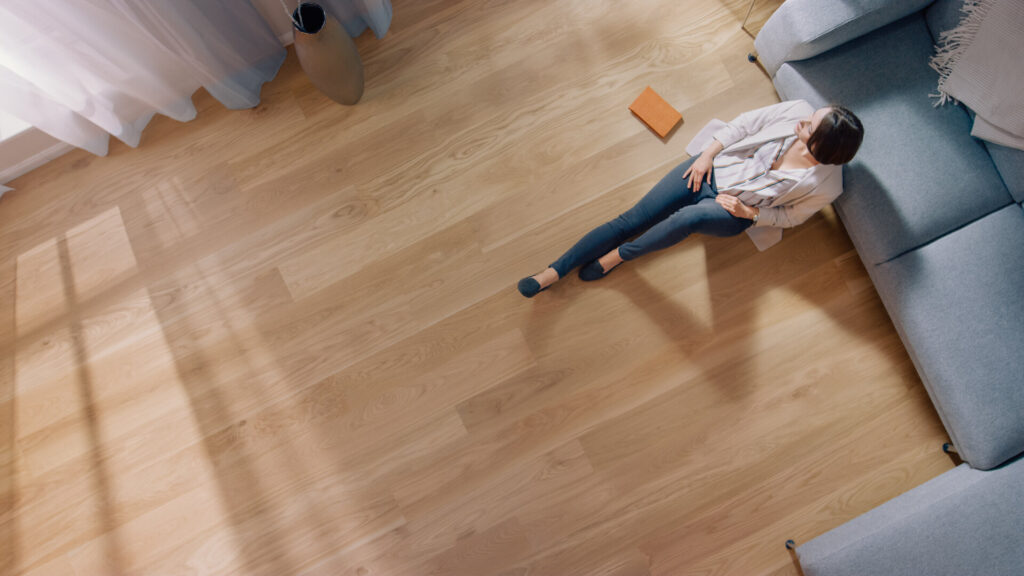 Junge Frau sitzt auf dem Boden im gemütlichen Wohnzimmer, mit modernem Interieur, grauem Sofa und Holzfußboden.