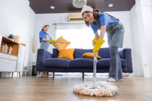 Reinigungsdienste wischen Boden und entfernen Staub vom Sofa im Wohnzimmer, Gruppe von Hausmädchen, Arbeiterinnen mit Handschuhen arbeiten, Reinigungsdienst-Konzept
